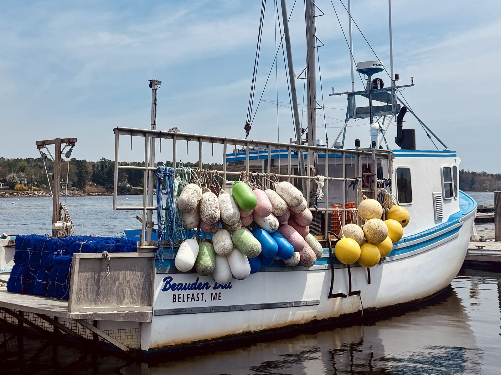 A white lobster boat at the dock in Belfast, Maine, hung with weathered buoys in pastel colors. Photograph by Christopher Kulawik.