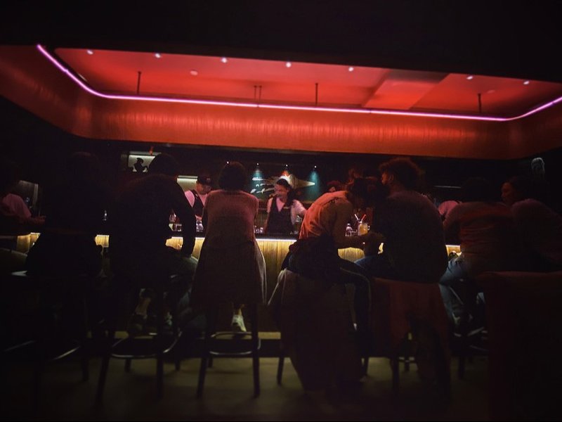 Silhouetted guests on stools at the bar of Double Chicken Please on the Lower East Side, under a glowing red ceiling ringed with pink neon. Photograph by Christopher Kulawik.