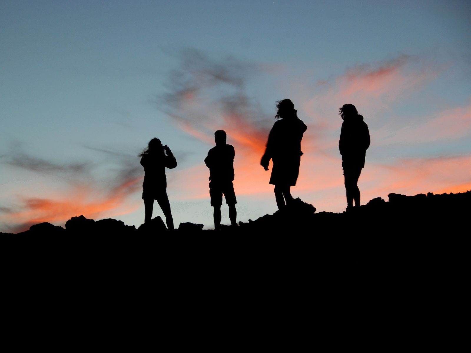 Four people silhouetted on the rocks of the Haleakalā summit against a sunset sky. Photograph by Christopher Kulawik.
