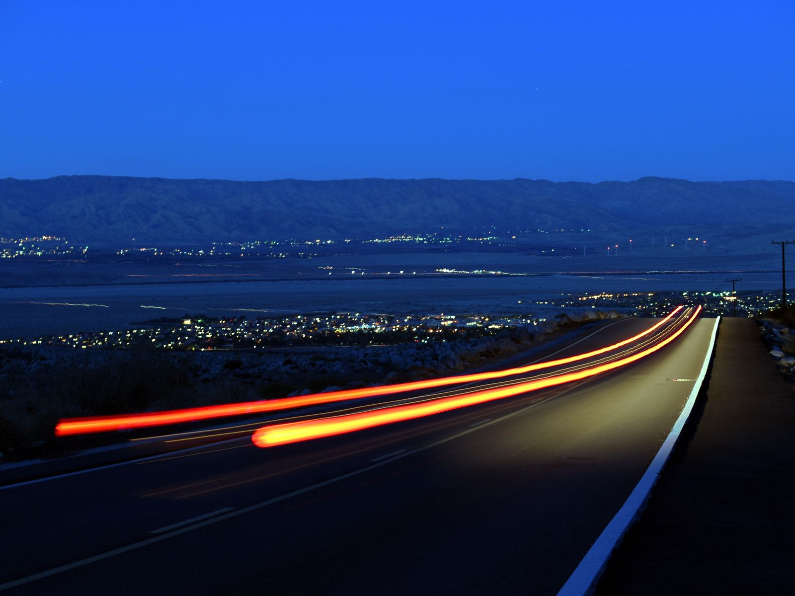 Tail-light trails on the road up to the Palm Springs Aerial Tramway at dusk, the lights of the Coachella Valley below. Photograph by Christopher Kulawik.