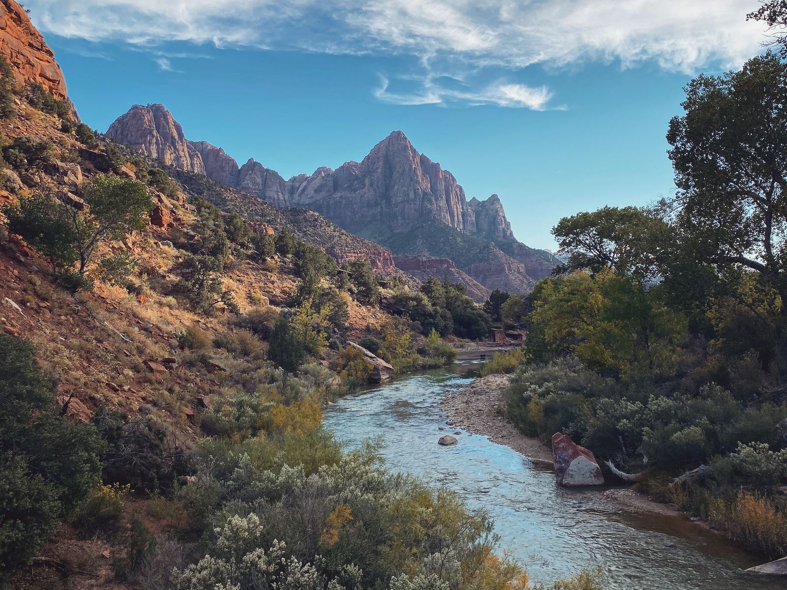 The Virgin River winding through desert scrub toward the Watchman peak in Zion National Park under a sky of streaked cloud. Photograph by Christopher Kulawik.